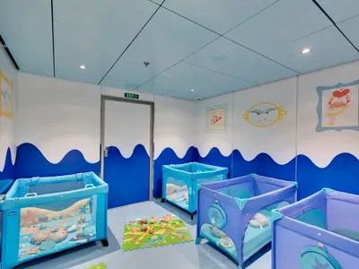 Der Baby Club Chicco an Bord der MSC Meraviglia zeigt blaue Babybetten und eine Spielmatte. Blau-weiße Wände mit Comic-Bildern.