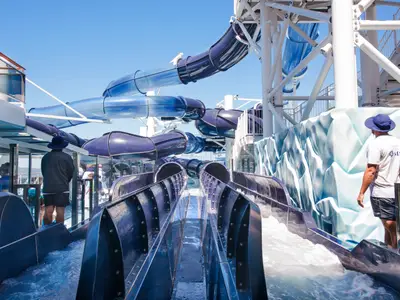 Blick auf den Polar Aquapark der MSC Meraviglia mit mehreren Wasserrutschen in verschiedenen Blautönen. Zwei Crew-Mitglieder sind am Beckenrand zu sehen, einer davon mit "MSC"-Shirt.
