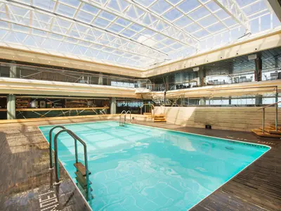 Der geräumige 'Bamboo Pool' auf der MSC Meraviglia, ein Innenpool mit transparentem Glasdach. Umgeben von Holz und Marmor, mit Bar und mehreren Decks.
