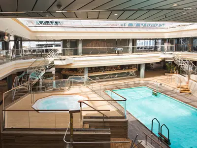 Das helle Atrium der MSC Meraviglia zeigt den großen Bamboo Pool, einen Whirlpool und eine elegante Bar auf der mittleren Ebene. Moderne Architektur mit Glas und Holz.
