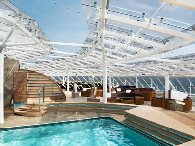 Panoramablick auf den eleganten Poolbereich des MSC Yacht Clubs an Bord der MSC Meraviglia mit Glasdach, Liegeflächen, Sitzgruppen und Meerblick.