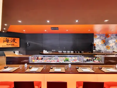 Innenansicht der Kaito Sushi Bar an Bord der MSC Meraviglia. Eine Theke zeigt frischen Fisch. Markante orangefarbene Decke und japanische Fächer-Tapete prägen das Interieur. Sitzplätze an der Bar.