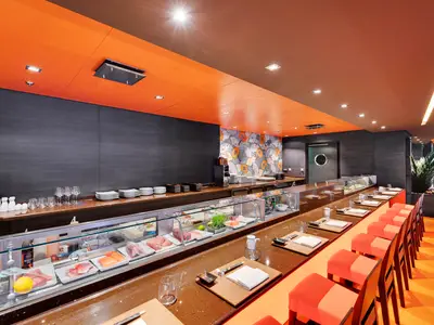 Blick in die moderne Kaito Sushi Bar an Bord der MSC Meraviglia. Eine lange Theke mit einer Kühlvitrine voller frischem Fisch und Sitzgelegenheiten mit orangefarbenen Hockern säumt den Raum.