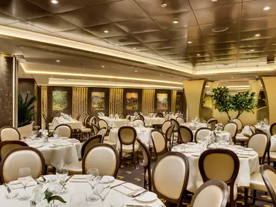 Das stilvolle Restaurant L'Olivo D'Oro an Bord der MSC Meraviglia zeigt Reihen von weiss gedeckten Tischen mit eleganten Stühlen, bereit für Gäste. An den Wänden hängen Gemälde.