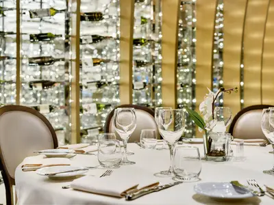 Ein elegant gedeckter Restauranttisch an Bord der MSC Meraviglia. Weiße Tischdecke, Gläser, Besteck und eine Orchidee. Im Hintergrund beleuchtete Weinregale.