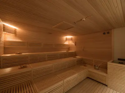 Helle, moderne Sauna im MSC Aurea Spa an Bord der MSC Meraviglia. Der leere Raum verfügt über gestufte Holzbänke, warme, indirekte Beleuchtung, einen Saunaeimer und den Ofen.