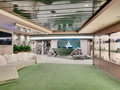 Der moderne Empfangsbereich des MSC Aurea Spa an Bord der MSC Meraviglia mit geschwungener Sitzbank, einem Fels-Design-Tresen und einem beleuchteten Yoga-Symbol an der Wand. Rechts sind Verkaufsregale mit Produkten zu sehen.