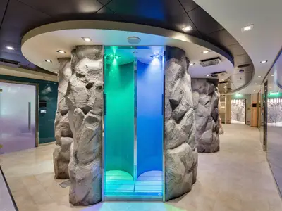 Blick in den futuristischen MSC Aurea Spa der MSC Meraviglia mit Felswänden und beleuchteten Erlebnisduschen in Grün und Blau. Ein beruhigender Ort für Wellness und Entspannung.