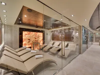 Blick in den hell erleuchteten Salt Relax Raum des MSC Aurea Spa an Bord der MSC Meraviglia mit mehreren Liegen und einer hinterleuchteten rosa Salzwand.