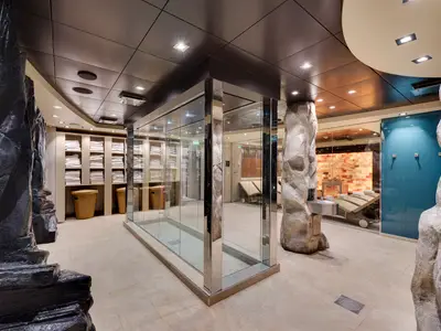 Ein luxuriöser Spa-Bereich an Bord der MSC Meraviglia. Im Vordergrund sind Felsformationen und eine große Glaskabine zu sehen. Im Hintergrund ist eine beleuchtete Salzsteinwand und Liegen sichtbar.