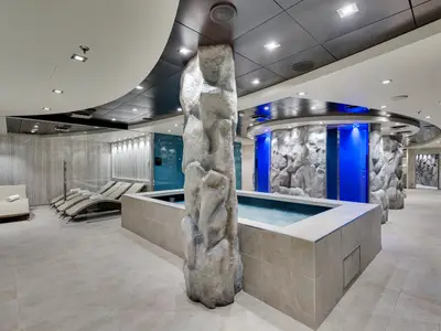 Ein luxuriöser Spa-Bereich an Bord der MSC Meraviglia. Mit Pool, großer Felsensäule, Entspannungsliegen und blau beleuchteten Felswänden im modernen Design.