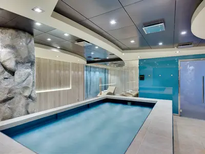 Das moderne MSC Aurea Spa an Bord der MSC Meraviglia zeigt einen beheizten Innenpool, Liegen und stilvolle Glaswände. Eine felsähnliche Säule prägt den linken Bereich.