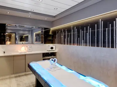 Ein moderner Spa-Behandlungsraum an Bord der MSC Meraviglia. Zu sehen sind ein Waschbeckenbereich mit Spiegel, eine Salzlampe und ein Massagebett mit blauer Unterbeleuchtung und Handtuch-Schwänen.