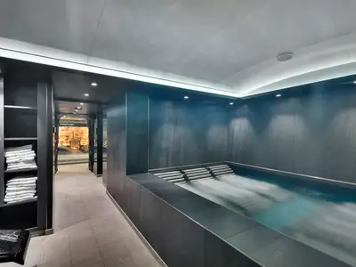 Ein modernes Spa an Bord der MSC Meraviglia mit Hydrotherapie-Pool, dunklen Wänden und einem angrenzenden Salzraum. Weiße Handtücher sind in Regalen gestapelt.
