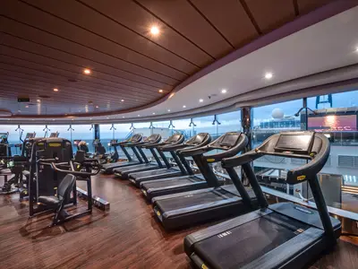 Modernes Fitnessstudio an Bord der MSC Meraviglia mit Technogym-Laufbaendern und Geraeten. Grosse Fenster bieten Meerblick auf das Oberdeck, ohne Personen.