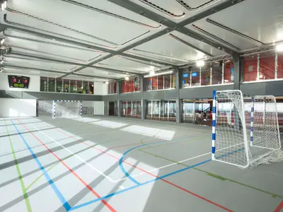 Der Sportplex an Bord der MSC Meraviglia: Heller, leerer Indoor-Sportplatz mit farbigen Linien, zwei Toren und Anzeigetafel. Grosse Fenster umgeben den Bereich.