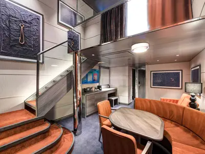 Die luxuriöse MSC Yacht Club Duplex Suite an Bord der MSC Meraviglia. Ein zweistöckiger Wohnbereich mit orangefarbener Sitzbank, Tisch, Kaffeebar und eleganter Treppe zur oberen Etage.