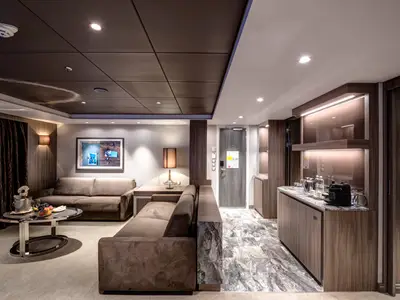 Helles, elegantes Wohnzimmer einer Royal Suite an Bord der MSC Meraviglia mit zwei grauen Sofas, einem Couchtisch mit Sektkühler, Obst und Gläsern, sowie einer Minibar und einem Holzboden.