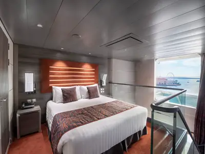 Blick in eine moderne, zweistöckige Duplex Suite der MSC Meraviglia mit Doppelbett, Treppe und bodentiefem Fenster mit Meerblick, ein Hafen mit Riesenrad ist zu sehen.