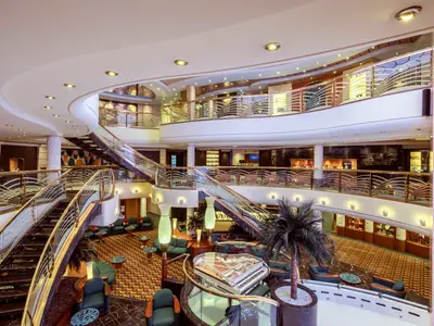 Das imposante Atrium der MSC Musica erstreckt sich über mehrere Ebenen mit geschwungenen Treppen, goldenen Balustraden und einem gläsernen Piano. Lounge-Bereiche laden zum Verweilen ein.