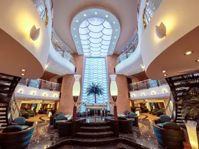 Das elegante Atrium der MSC Musica mit geschwungenen Balkonen und zentraler Fischschuppen-Lichtinstallation. Gemütliche Sitzbereiche laden zum Verweilen ein.