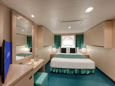 Geräumige Aussenkabine der MSC Musica mit einem großen Doppelbett, grünen Vorhängen und einem runden Bullauge. Ein Schminktisch mit TV befindet sich links. Der Raum ist hell beleuchtet.
