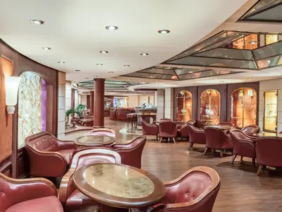 L'Enoteca Wine Bar an Bord der MSC Musica. Rote Ledersessel, Holztische, Bar und Vitrinen mit Glaswaren prägen den eleganten Raum. Warmes Licht, dunkles Holz.