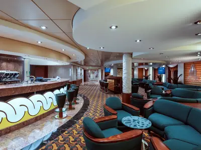 Innenansicht der Bar della Cascata an Bord der MSC Musica. Eine lange, geschwungene Bar, Barhocker und ein grosszuegiger Loungebereich mit blauen Sofas und Sesseln sind zu sehen.