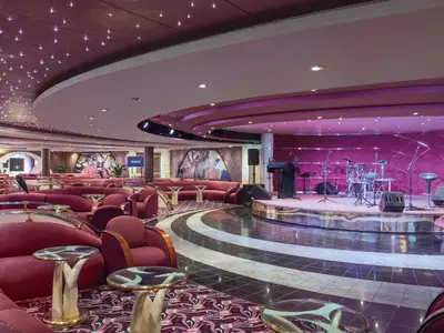 Il Tucano Lounge auf der MSC Musica. Bühne mit Schlagzeug und Mikrofonen. Rote Sofas und Sessel. Sternenlichtdecke und Vogelkunst.