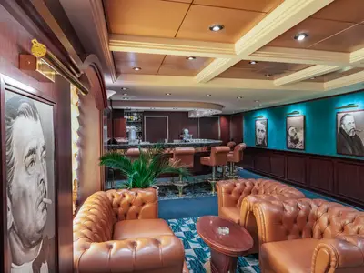 Innenansicht des Havana Club an Bord der MSC Musica, einer eleganten Zigarrenlounge mit einer geschwungenen Bar, braunen Ledersesseln und Wandbildern an einer tuerkisen Wand.