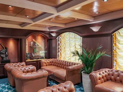 Ein luxuriöser Innenraum der Havana Club Lounge an Bord der MSC Musica mit braunen Chesterfield-Ledersofas, dunkler Holzvertäfelung, Vitrinen und Pflanzen. An der Wand hängt eine Skulptur einer Hand, die eine Zigarre hält.