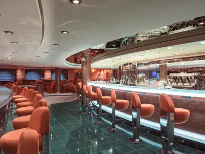 Die elegante Bar-Lounge an Bord der MSC Musica. Eine geschwungene Bar mit leuchtender Theke und orangefarbenen Barhockern. Dahinter gemütliche Sitzgruppen mit Sesseln.