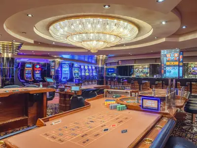 Casino Sanremo an Bord der MSC Musica. Im Vordergrund ein Roulette-Tisch mit Chips. Dahinter beleuchtete Spielautomaten und eine Bar. Eine grosse Kristallleuchte schmückt den Raum.