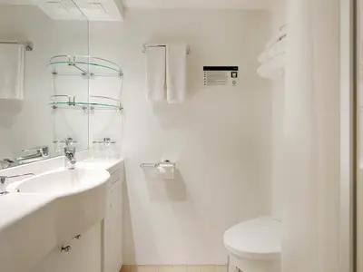 Modernes Badezimmer einer Kabine auf der MSC Musica. Mit Waschbecken, Spiegel, Glasablagen, Handtüchern, Toilette und Duschvorhang. Helle, saubere Einrichtung.