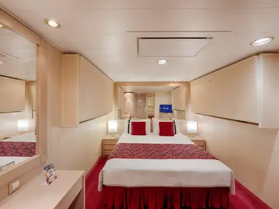 Eine komfortable Innenkabine an Bord der MSC Musica. Ein Doppelbett mit roten Kissen und einer roten Bettdecke ist zentral platziert. Zwei Nachttische mit Lampen stehen daneben, der Boden ist mit rotem Teppich ausgelegt. Ein Spiegel und ein Fernseher sind gegenüber dem Bett.