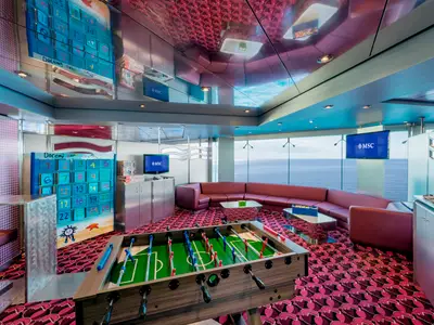 Ein farbenfroher Junior Club an Bord der MSC Musica mit großen Fenstern mit Meerblick. Im Vordergrund steht ein Foosballtisch. Ein großes, nummeriertes Doremi-Spielbrett ist an der Wand zu sehen. Rote Sitzbänke säumen die Fensterfront.