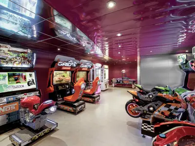 Arcade an Bord der MSC Musica mit Rennspiel-Automaten: Motorrad- und Auto-Simulatoren. Eine Greifmaschine und ein Airhockey-Tisch im Hintergrund. Heller, modern gestalteter Raum.
