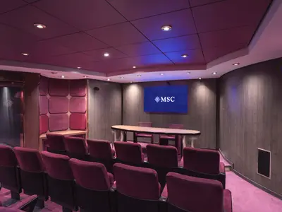Der elegante Konferenzraum 'Sala Viola' an Bord der MSC Musica mit Reihen von burgunderroten Sitzen, einem langen Konferenztisch und einem großen Bildschirm mit MSC Logo an der Wand.