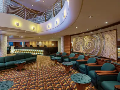 Die stilvolle Lounge und Rezeption an Bord der MSC Musica zeigt grüne Sofas und Sessel, einen farbenfrohen Teppich und ein grosses, goldenes Spiral-Kunstwerk an der Wand. Im Hintergrund ist der Empfangstresen zu sehen.