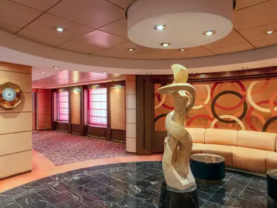 Blick in eine elegante Lounge der MSC Musica mit moderner Skulptur, beiger Sitzecke und Ringmuster an der Wand. Links ist ein Schild 'Timeless Studio' sichtbar.