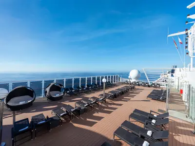 Das sonnige Sonnendeck der MSC Musica bietet zahlreiche schwarze Liegestühle und elegante Lounge-Pods mit Blick auf das weite, blaue Meer und den Horizont. Der Himmel ist wolkenlos.