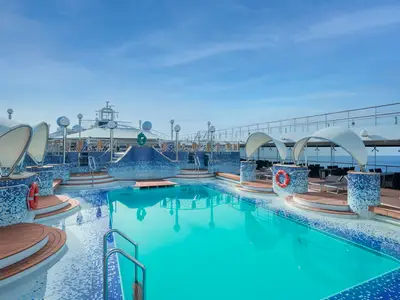 Einladender Aussenpoolbereich "La Spiaggia" an Bord der MSC Musica. Türkisfarbenes Wasser, blaue Mosaikfliesen, Holzdecks, Liegestühle und Sonnensegel unter blauem Himmel mit Meerblick.