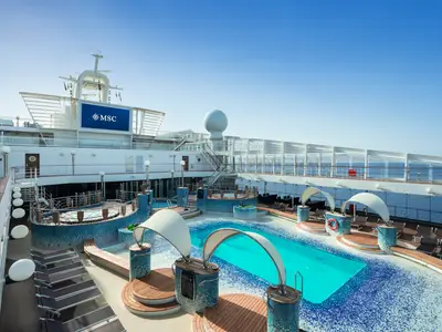 Blick auf das grosszügige Pooldeck der MSC Musica. Türkise Pools, Whirlpools und Liegestühle sind unter blauem Himmel arrangiert. Im Hintergrund sind das Meer und ein grosser MSC-Bildschirm zu sehen.