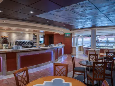 Innenansicht des eleganten Barbereichs an Bord der MSC Musica mit langer Marmortheke, Kaffeemaschinen, Flaschenregalen und vielen Tischen mit Stühlen, davor Meerblick.