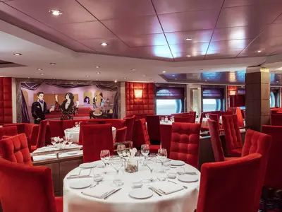 Elegantes Restaurant an Bord der MSC Musica mit roten Samtstühlen, weiß gedeckten Tischen und einem großen Wandgemälde im Belle Époque Stil. Runde Fenster bieten Meerblick.