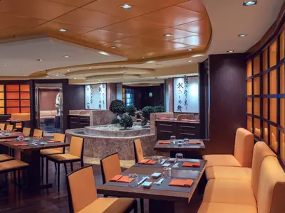 Das elegant eingerichtete japanische Spezialitätenrestaurant Kaito Sushi Bar an Bord der MSC Musica mit Tischen, Stühlen und einer zentralen Bepflanzung. Gedämpftes Licht schafft eine gemuetliche Atmosphäre.