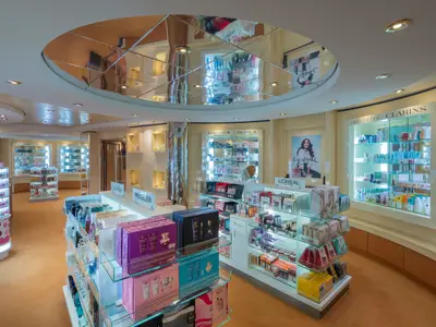 Die Le Parfum Boutique an Bord der MSC Musica. Beleuchtete Glasregale zeigen Parfüm und Kosmetik bekannter Marken. Der helle Shop hat eine verspiegelte Decke und orangefarbenen Teppich.