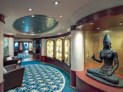 Blick in die elegante Lounge der MSC Musica mit Rattan-Sesseln, Schaufenstern und einer imposanten Statue vor goldener Mosaikwand. Im Hintergrund ein weiterer Bereich mit Meerblick.