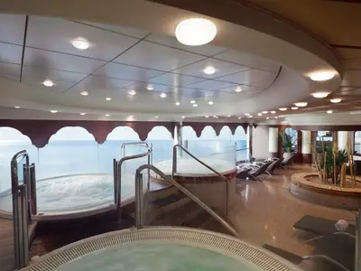 Blick in den eleganten Spa- und Wellnessbereich der MSC Musica mit mehreren sprudelnden Whirlpools, Liegestühlen und Meerblick durch große Fenster.