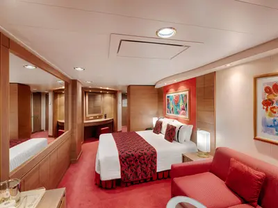 Helle Premium Suite Aurea an Bord der MSC Musica. Doppelbett, rotes Sofa, Schminkbereich. Roter Teppich und Holzvertäfelung.